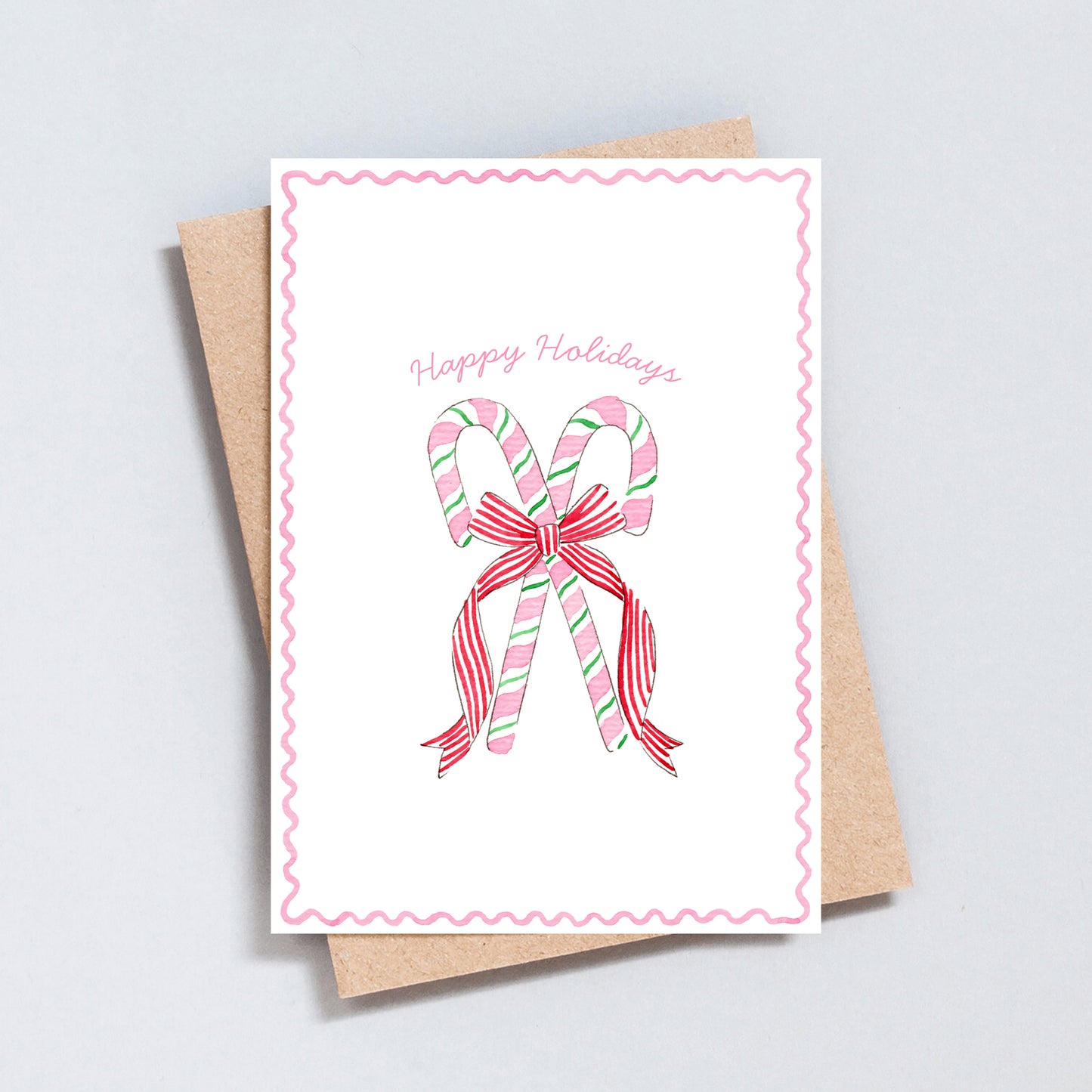 Pastel candy cane Christmas card with red and pink striped bow, illustrated by The Type Club, styled with kraft envelope.