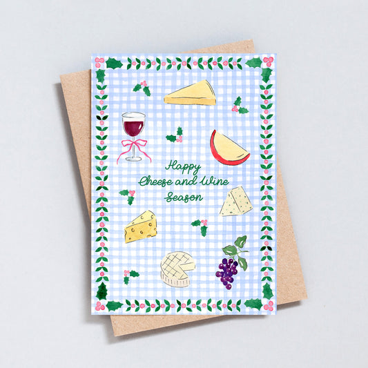 Illustrated Happy Cheese and Wine Season Christmas card featuring hand-painted cheeses, red wine, grapes and holly on a blue gingham background.