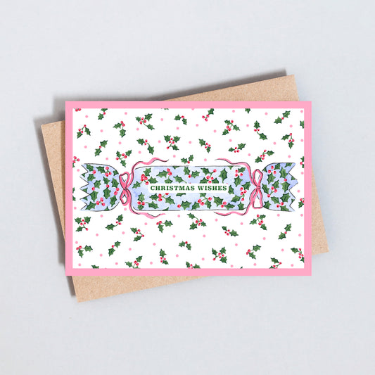 Christmas card featuring a traditional cracker decorated with holly, pink bows and Christmas Wishes lettering.