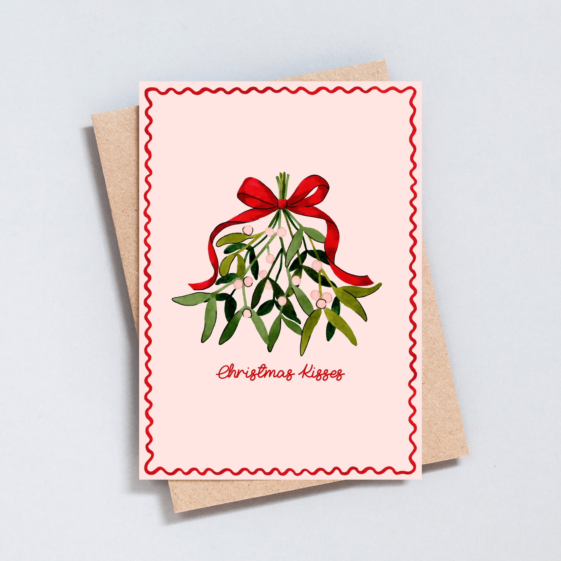 Christmas Kisses card featuring hand-painted mistletoe and red bow on pink background, festive greeting card printed on hammered 300gsm card.