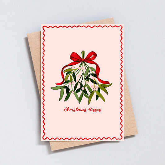 Christmas Kisses card featuring hand-painted mistletoe and red bow on pink background, festive greeting card printed on hammered 300gsm card.