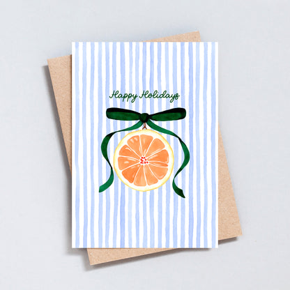 Happy Holidays card with hand-painted orange slice ornament and green ribbon on blue striped background