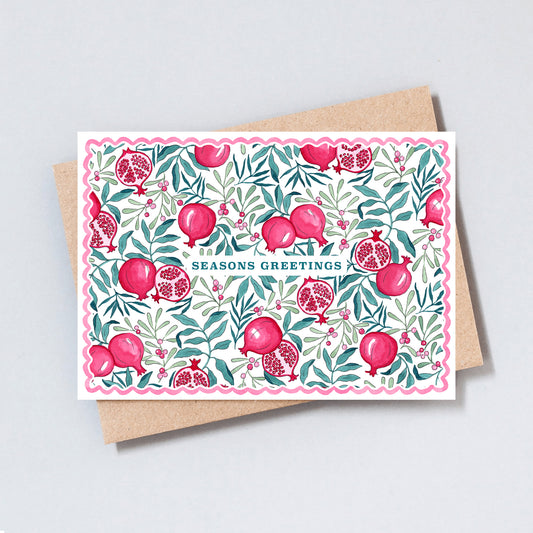 Illustrated Seasons Greetings Christmas card featuring hand-painted pomegranates, winter foliage and berries with a pink scalloped border.