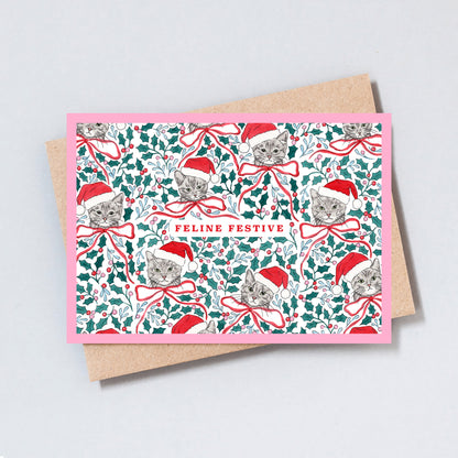 Illustrated Christmas card featuring cats wearing Santa hats amongst holly, festive foliage and ribbon bows with the words Feline Festive.
