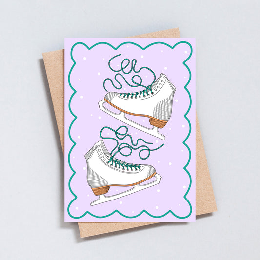 Hand illustrated Christmas card featuring white ice skates with green laces on a lilac background with scalloped edges.