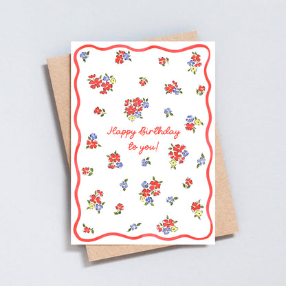 Minimal floral birthday card with scattered colourful flowers, pink script lettering and pink wavy border