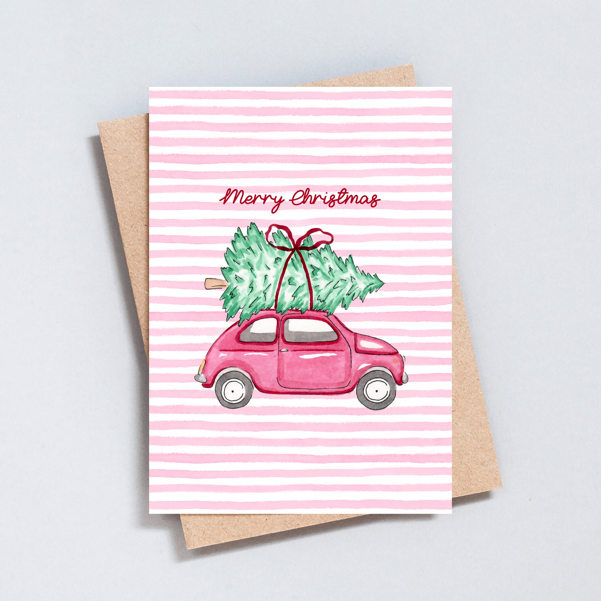 Cute Christmas card featuring a pink vintage car carrying a Christmas tree on a pink striped background.