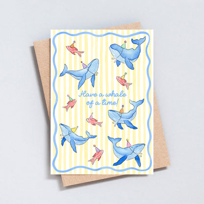 Cute whale birthday card with illustrated blue whales and colourful fish wearing party hats on a pale yellow striped background, with the message “Have a whale of a time!”
