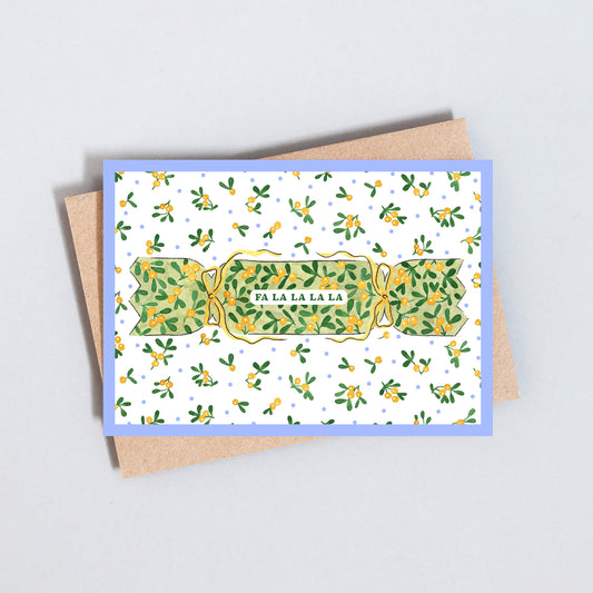 Illustrated Christmas card featuring a traditional Christmas cracker with festive greenery and Fa La La La greeting on textured white card.